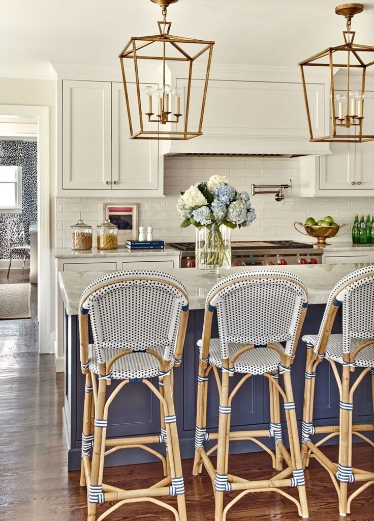 The kitchen at 19 South Portland — navy island, white cabinetry, brass lantern pendants, and bistro counter stools.